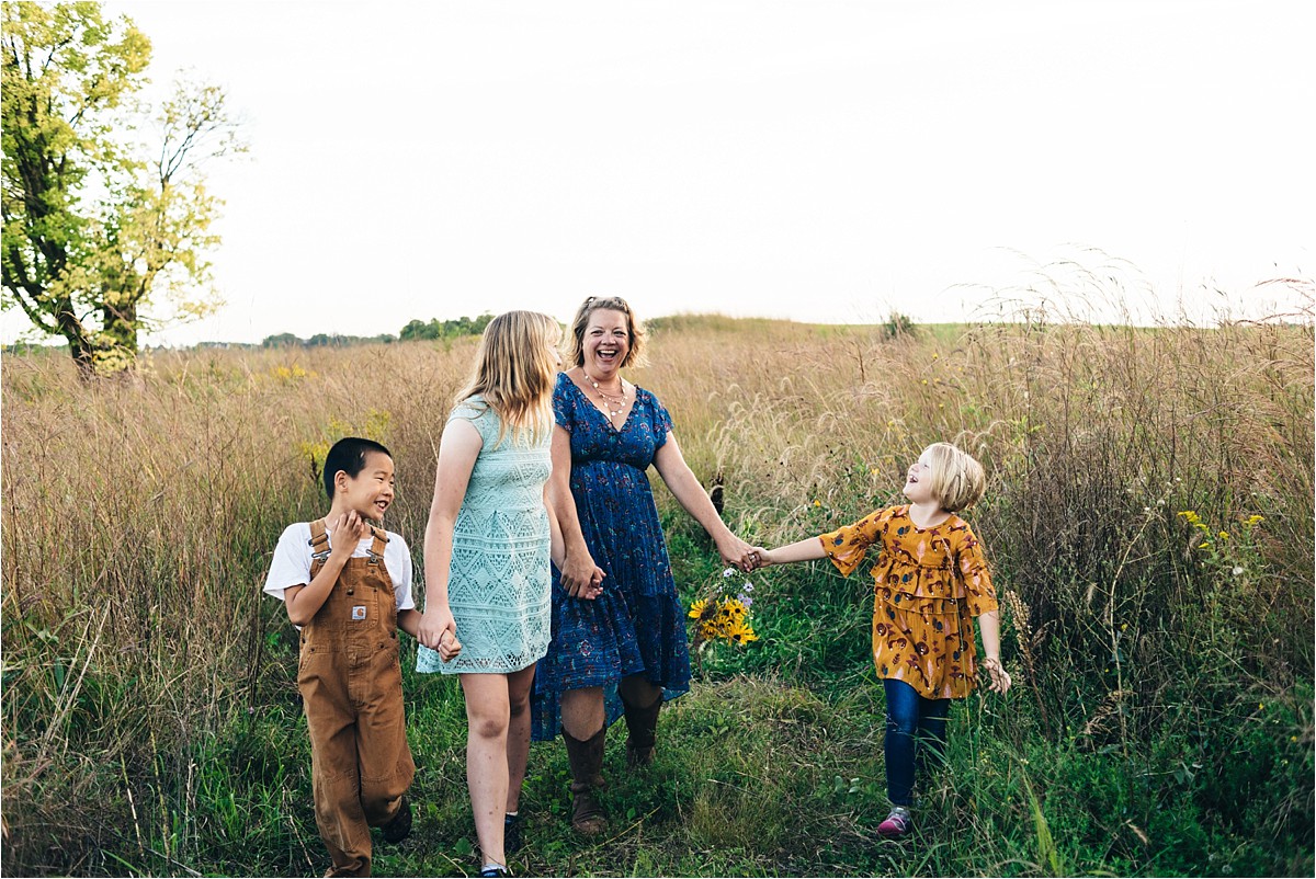 Mother and three kids hold hands and walk in a field at Bea Hive Farm.