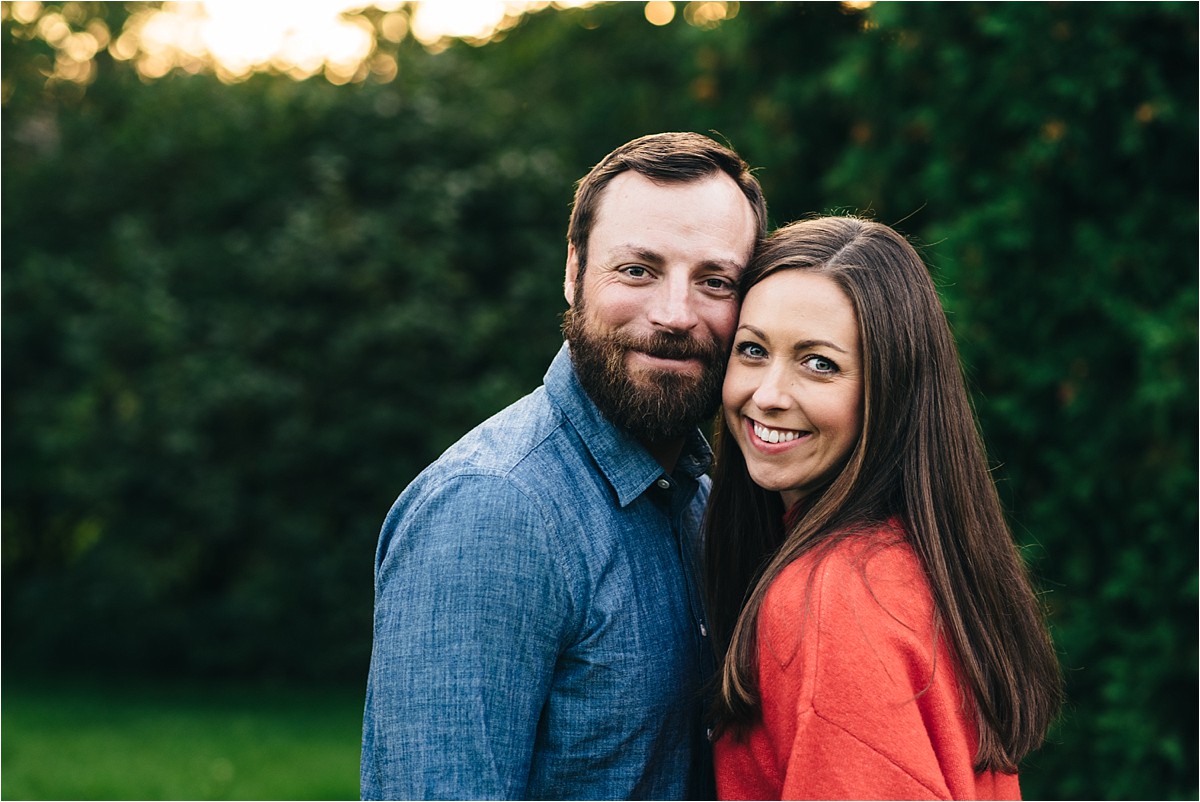 Couple poses for photo in a park, looking at camera smiling.