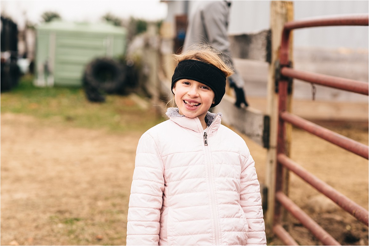 Little girl smiles at camera near horse pen.