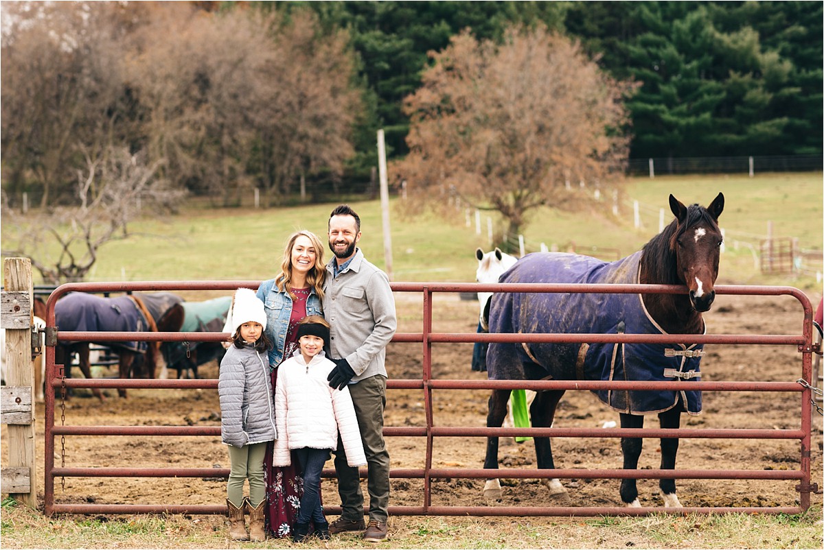 Family poses in front of horses for family photo.