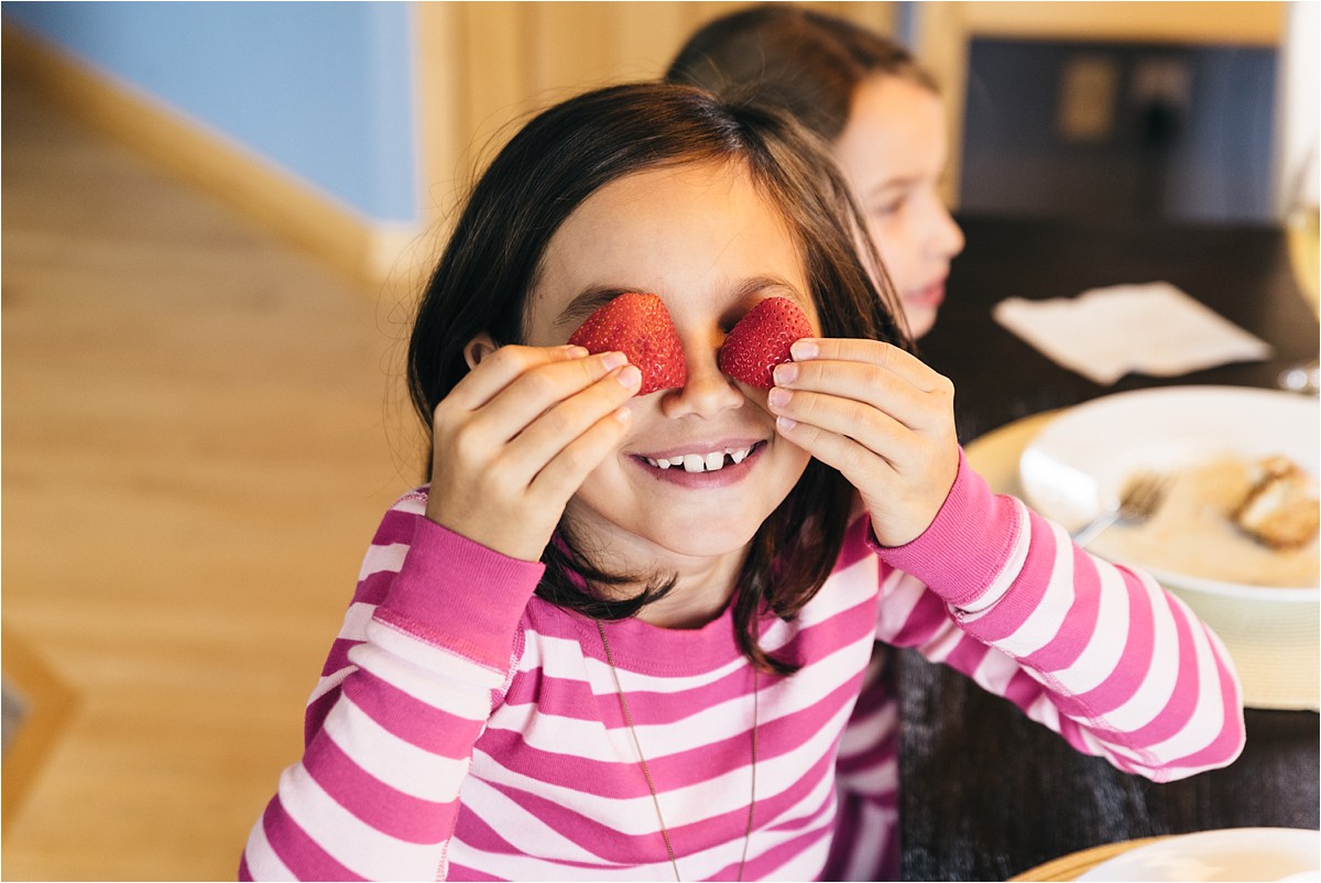 Young girl holds strawberries in front of her eyes.