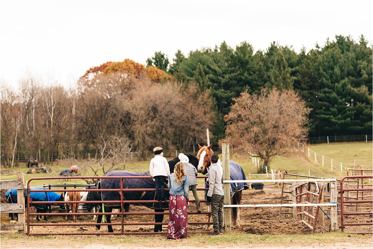 Family stands near fence of horse pen.