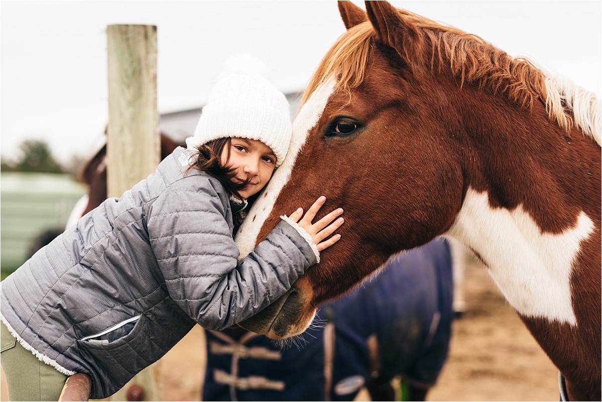 Young girl hugs horse.