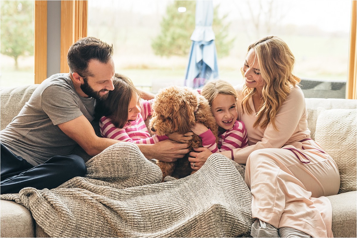 Family of four and dog sit on couch and snuggle laughing.