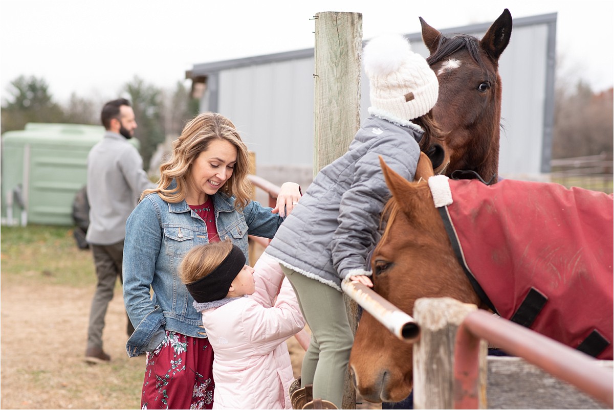 Little girl stands near family and horse, hugging it.