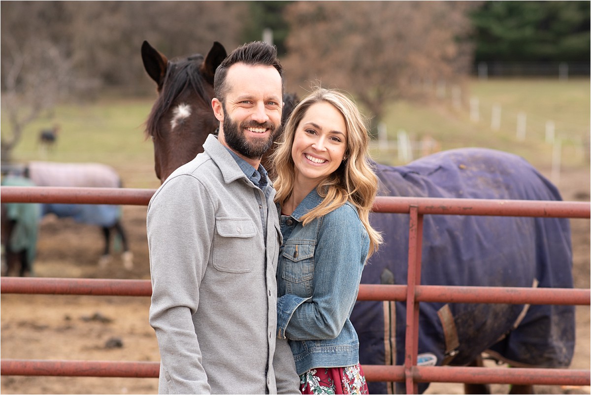 Couple stands near horses posing for photo.