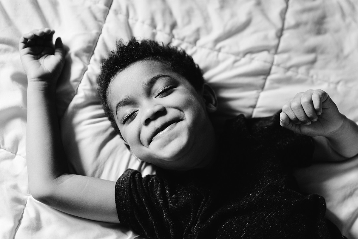 Black and white image of young boy smiling on bed.