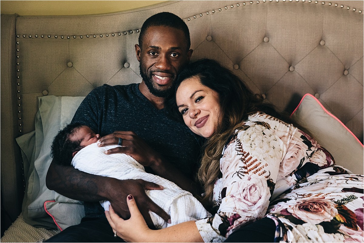 Mother and father smile at camera with newborn daughter.