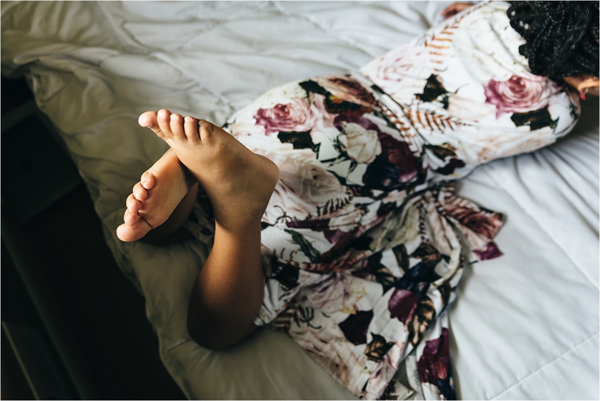 Girl's feel crossed in the air as she lays on her stomach on a bed.