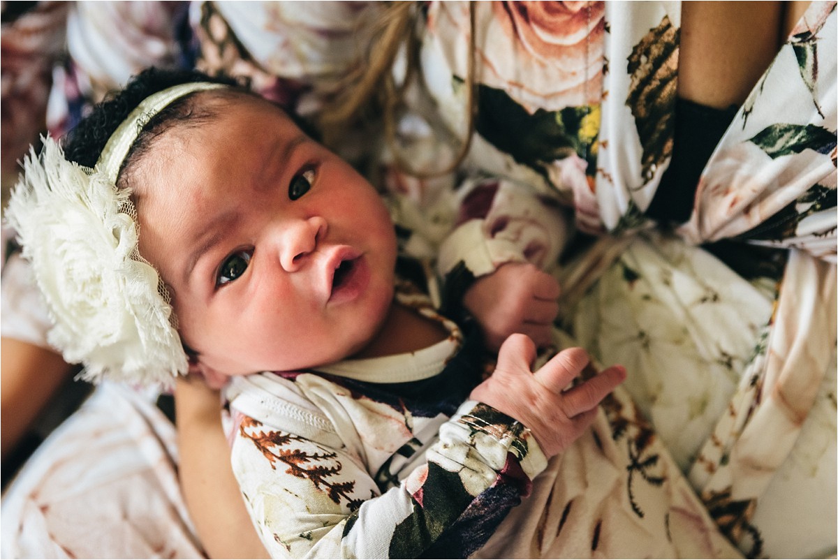 Newborn baby cradled in mothers arms looks up at camera.