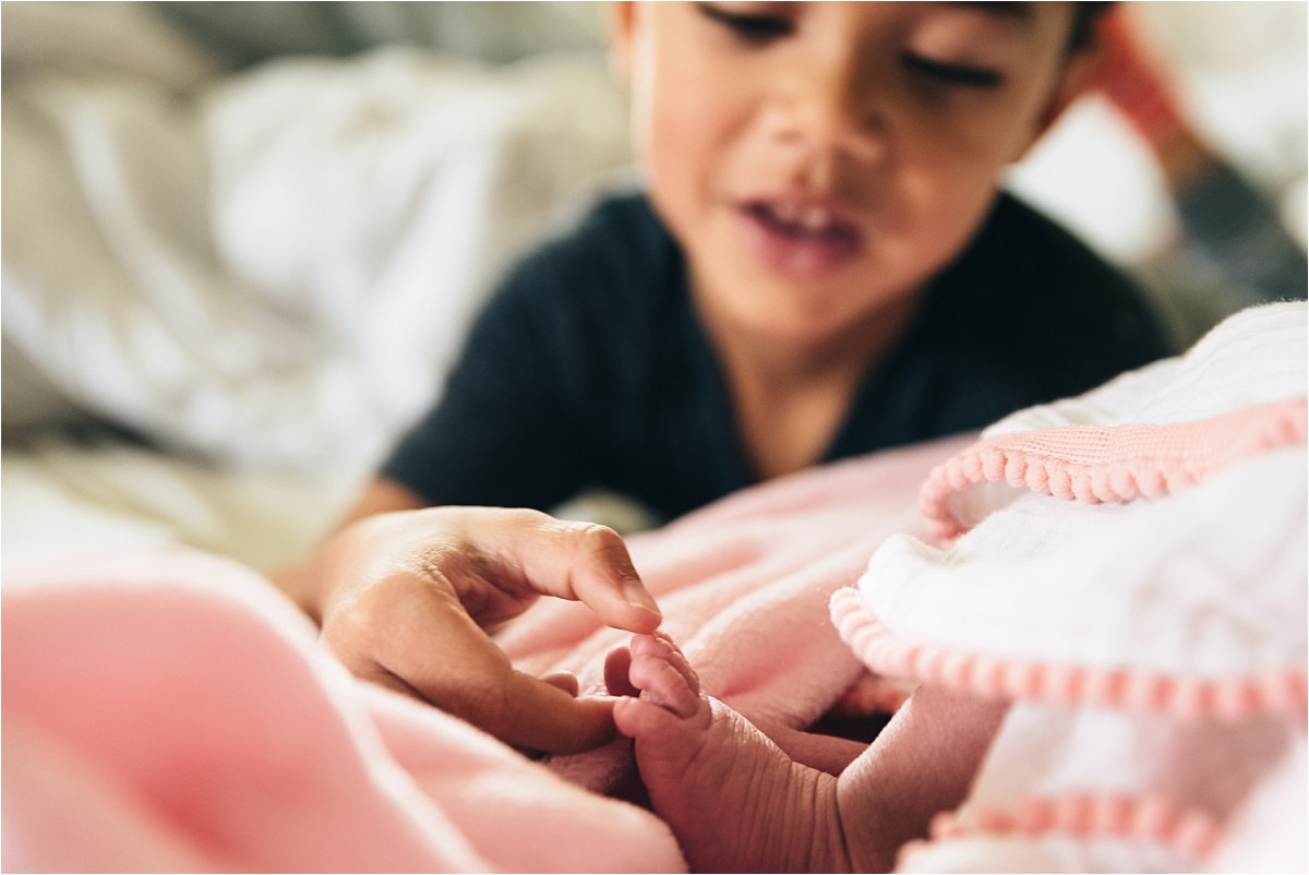 Young boy studies his new baby sister in newborn in-home photo session.