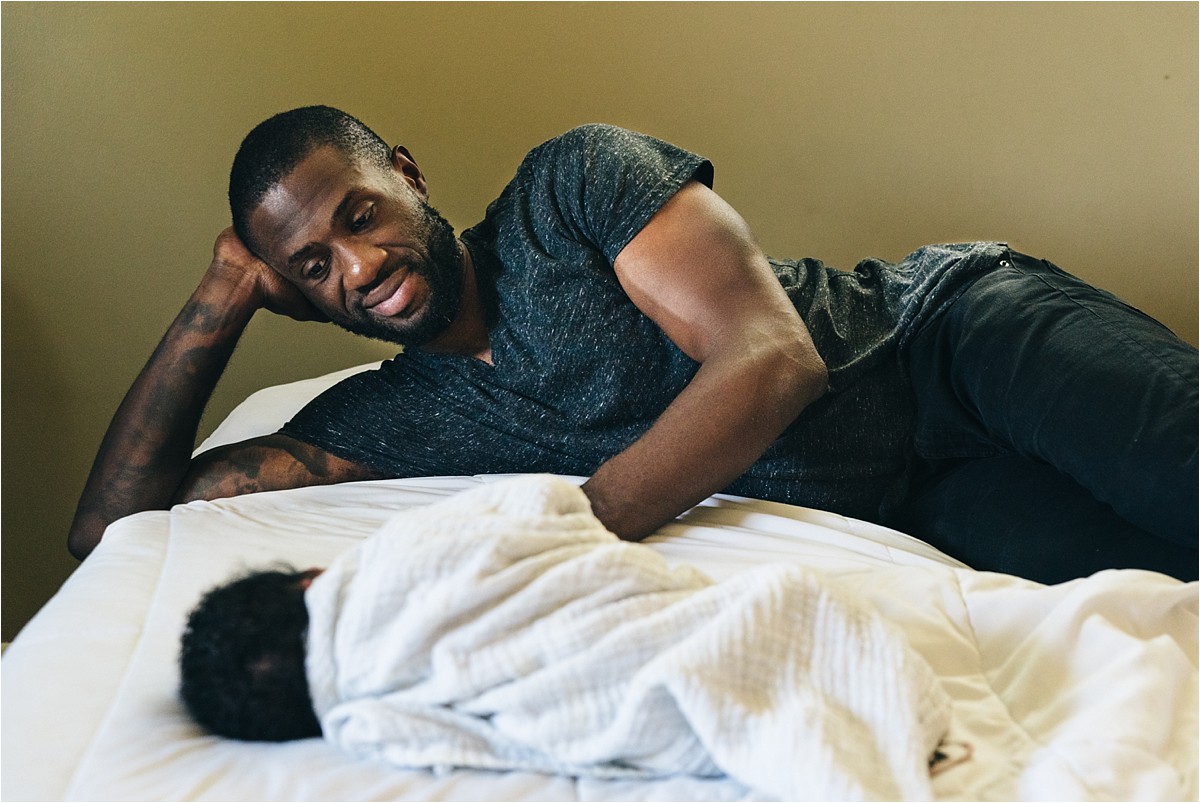 Father lays on bed and admires newborn daughter. in-home lifestyle newborn photography