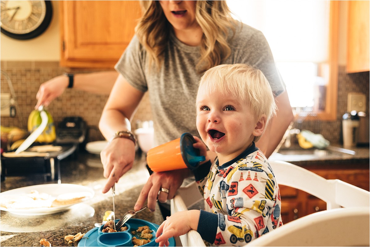 Young boy laughs while mother cuts pancake for him.