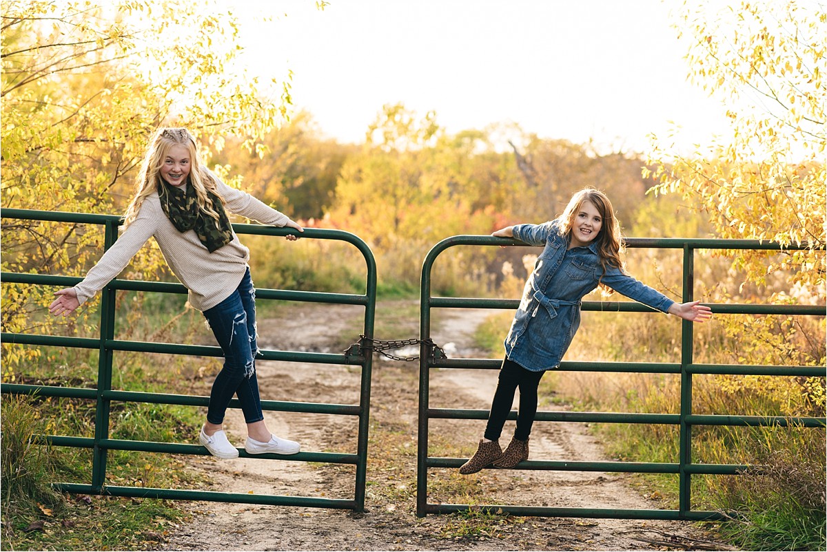 Sisters hang off cattle fence doors with arms outstreched.