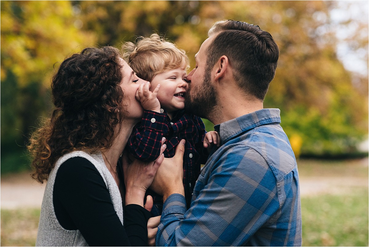 mother and father kiss little boy at park