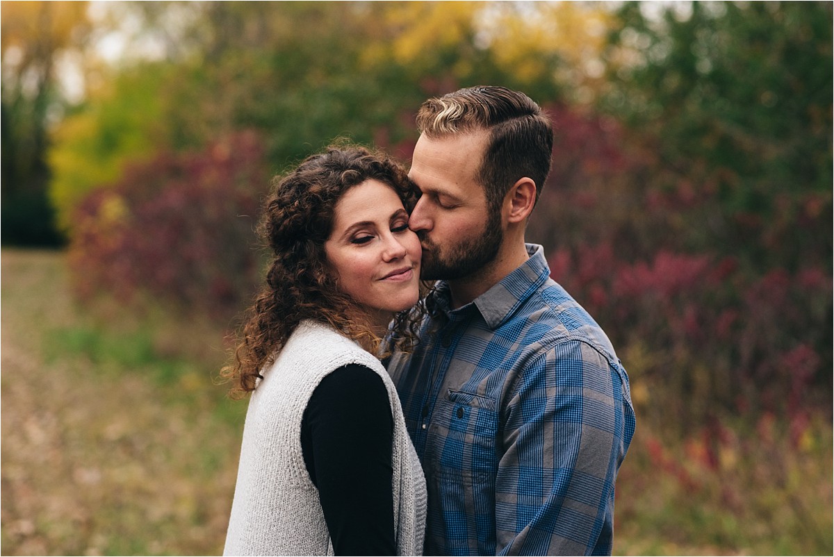 Husband kisses wife on the cheek in park.