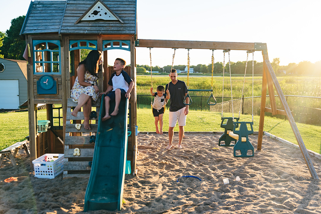 Family all plays on a swing set in the backyard.