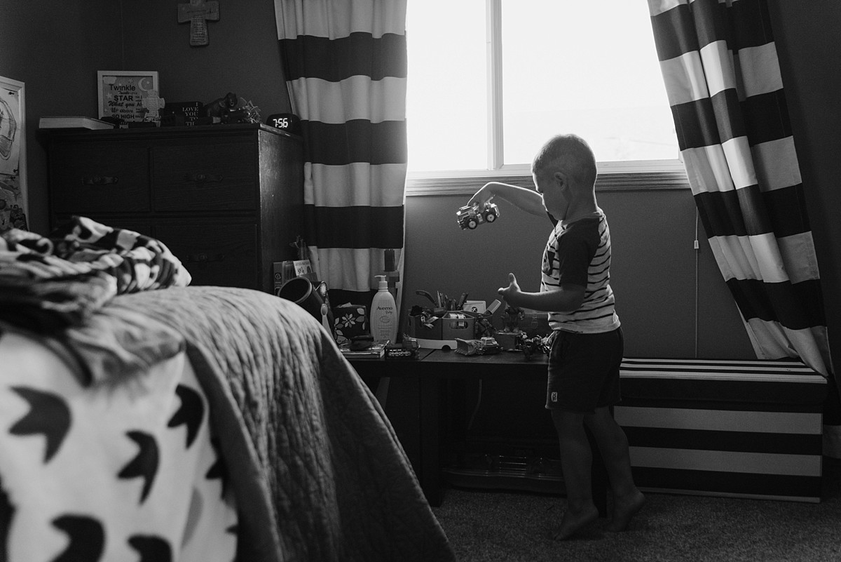 Black and white photo of boy playing with trucks in his room.