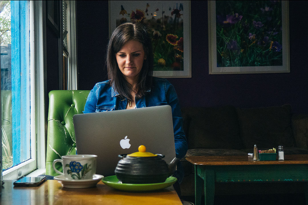 Woman sits in tea shop on computer, storing digital photos and videos.