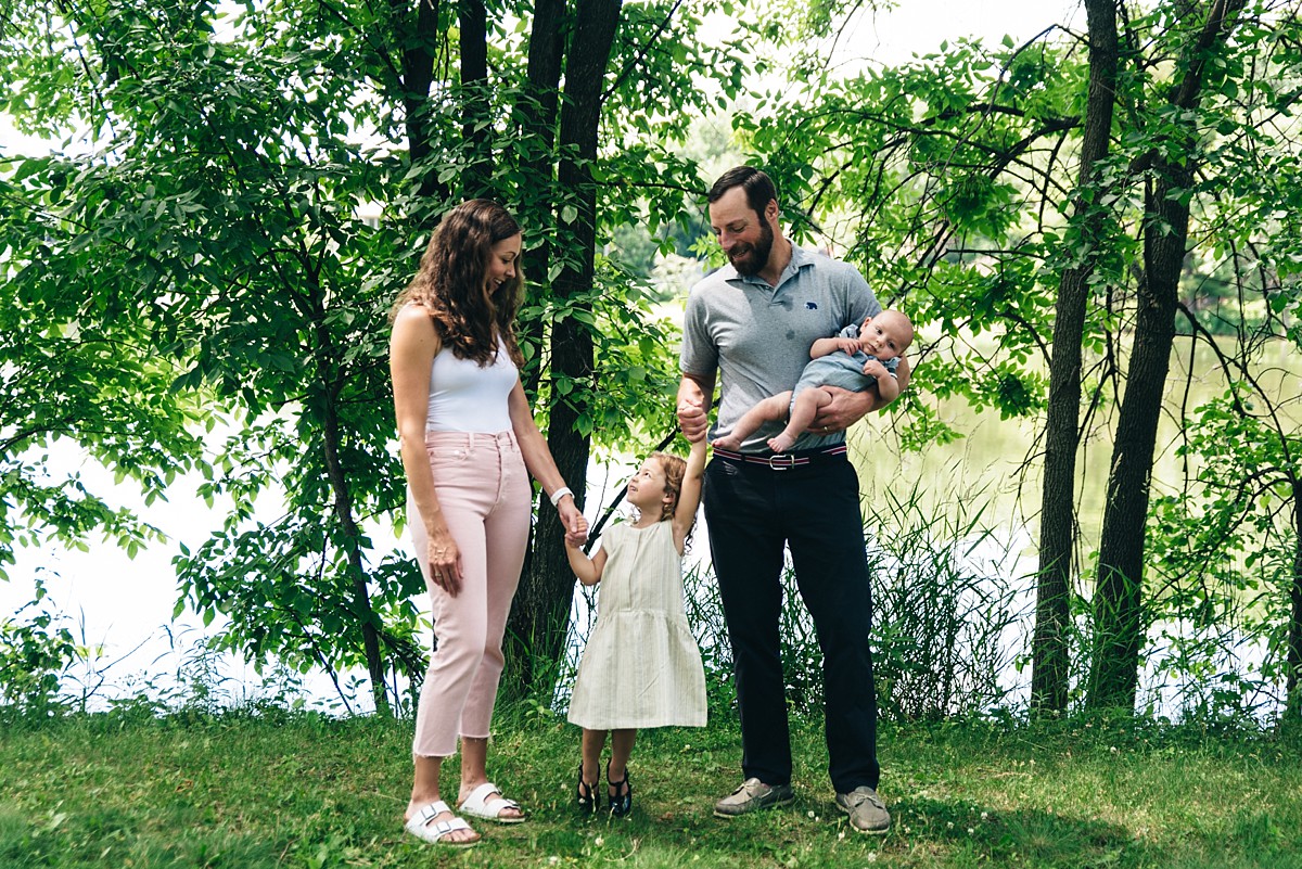 Family stands by lake holding hands.