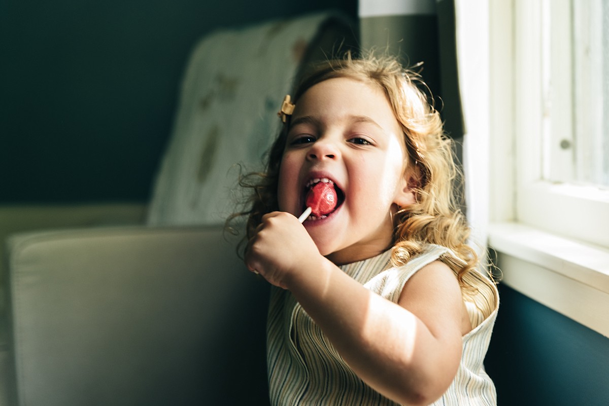 Little girl sits in room eating sucker during full family film.