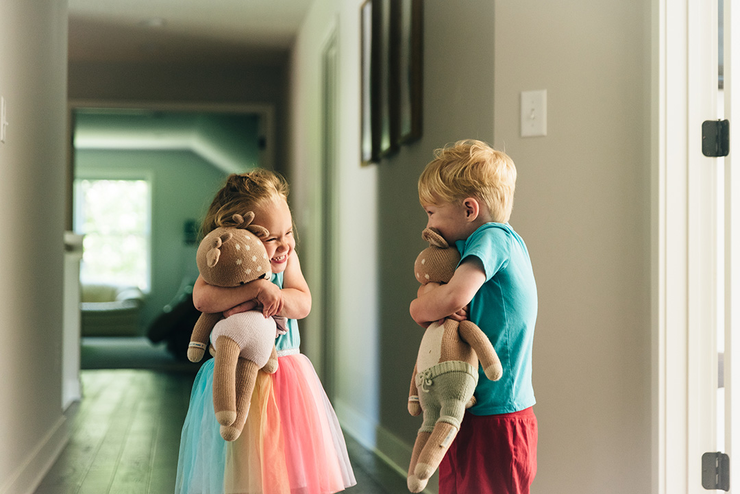 Three year old twins hold their stuffed animals in a hallway.