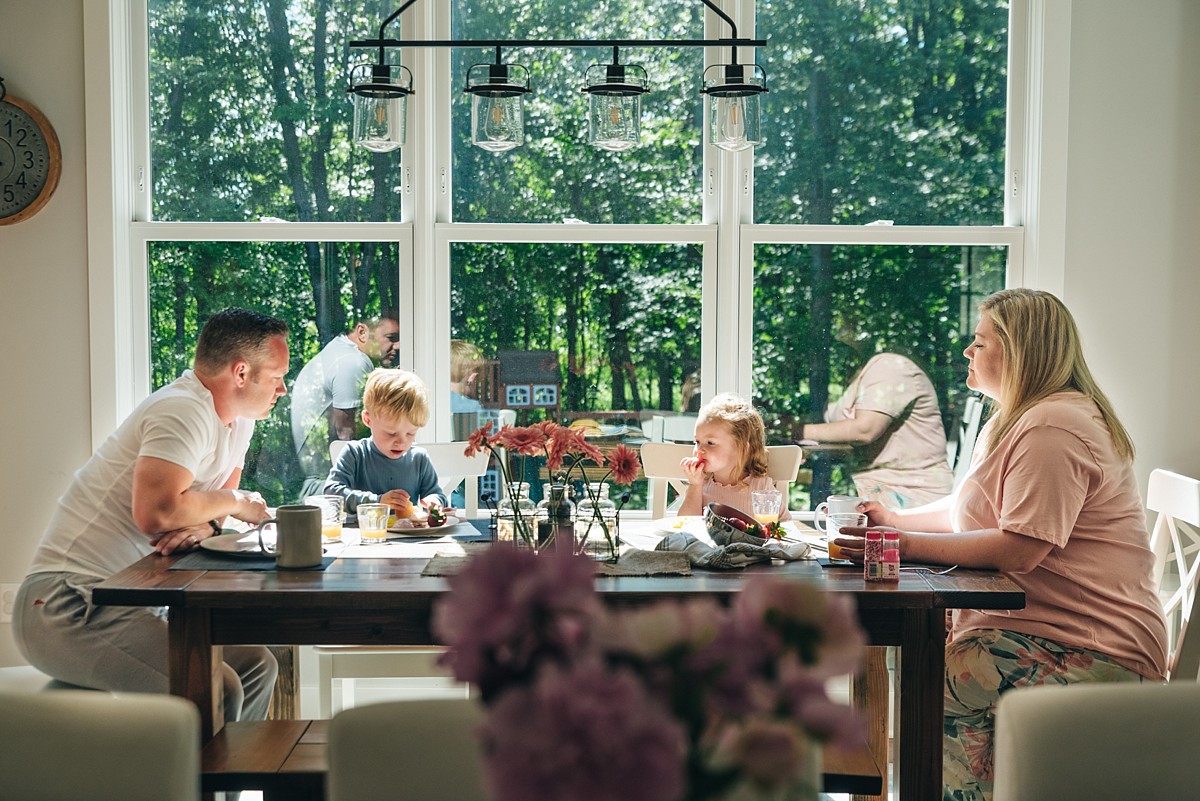 Family of four sits at the kitchen table eating breakfast and talking.