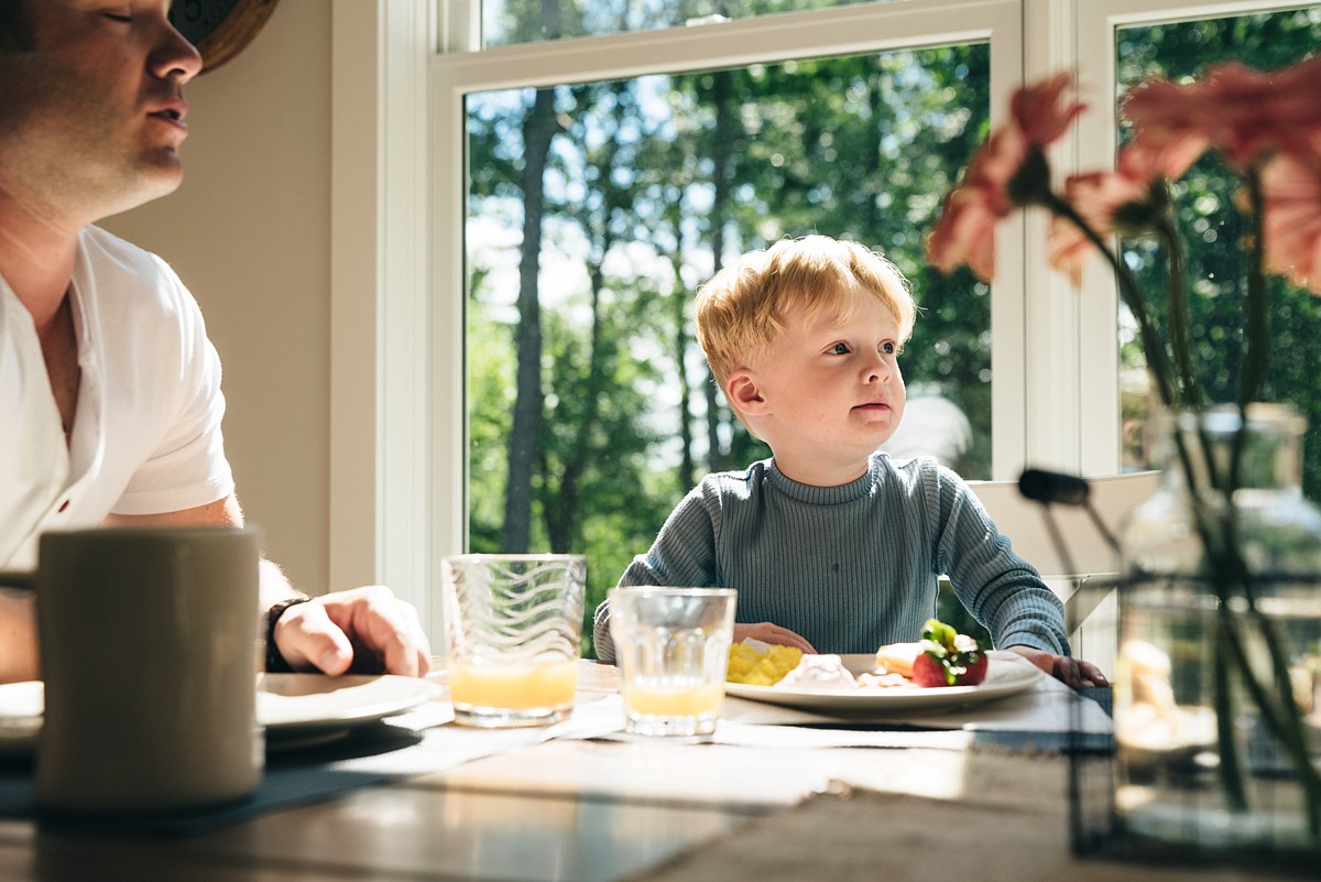 Little boy sits at table eating breakfast during Minnesota family video.