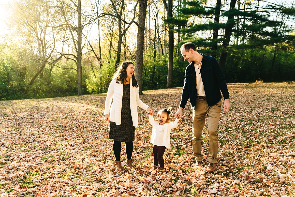 Family of three holds hands and walks through park.