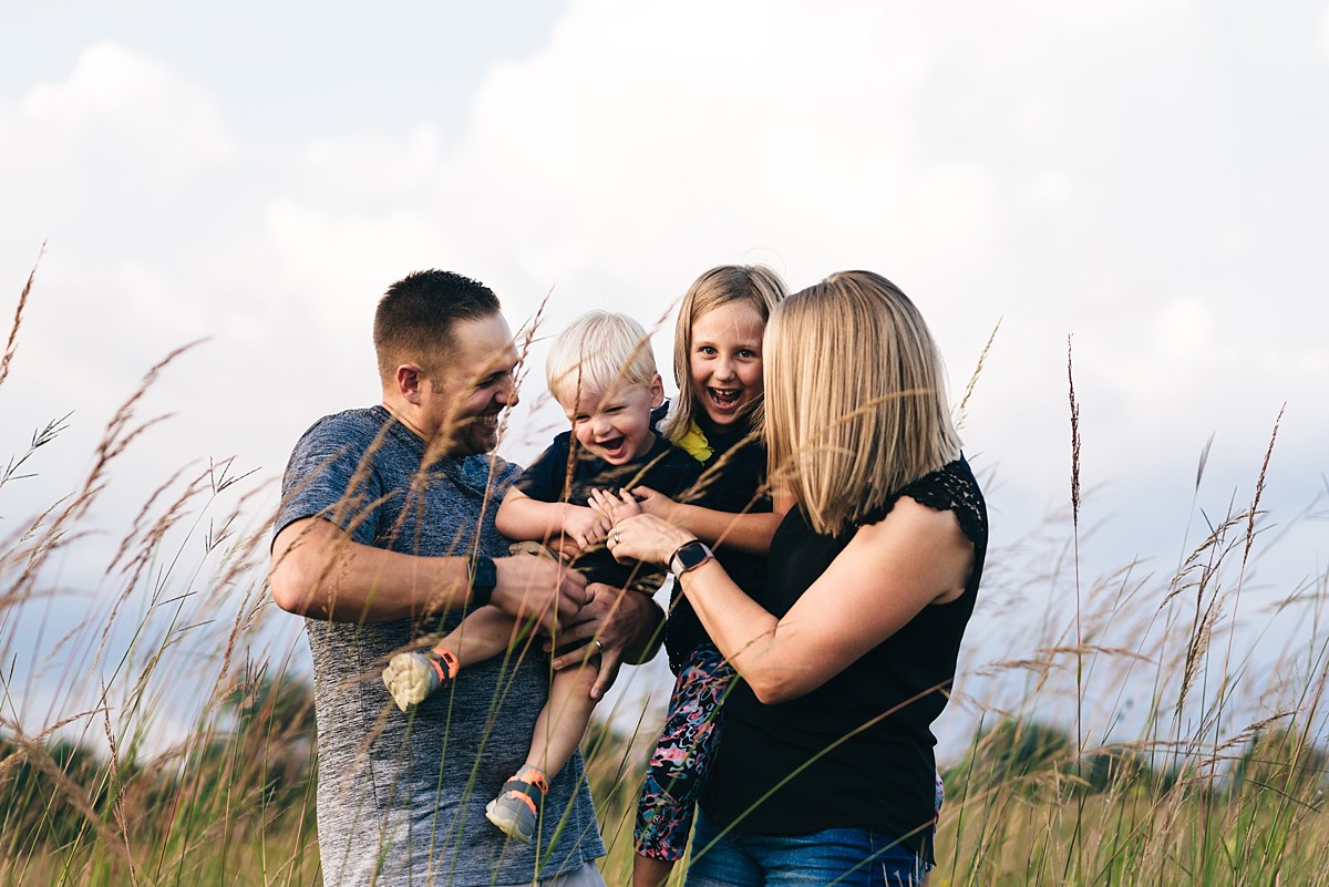 Family of four tickles each other in a field of tall grass.