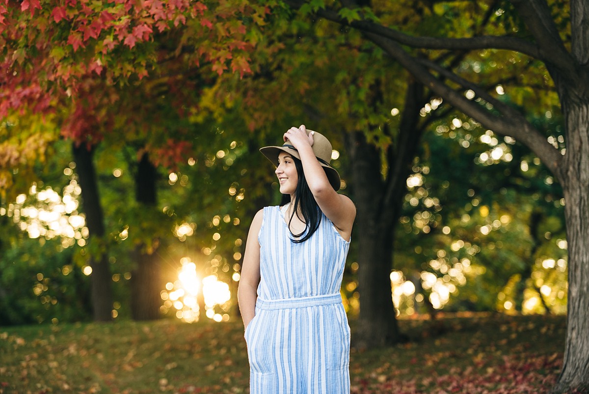 Teenage girl holds hat to her head during Minnesota sunset photography session.