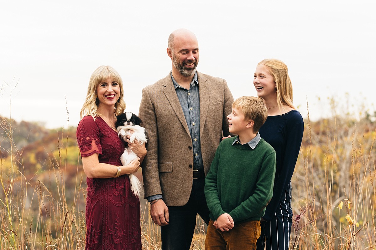 Family with adolescent kids stands in a field petting dog.