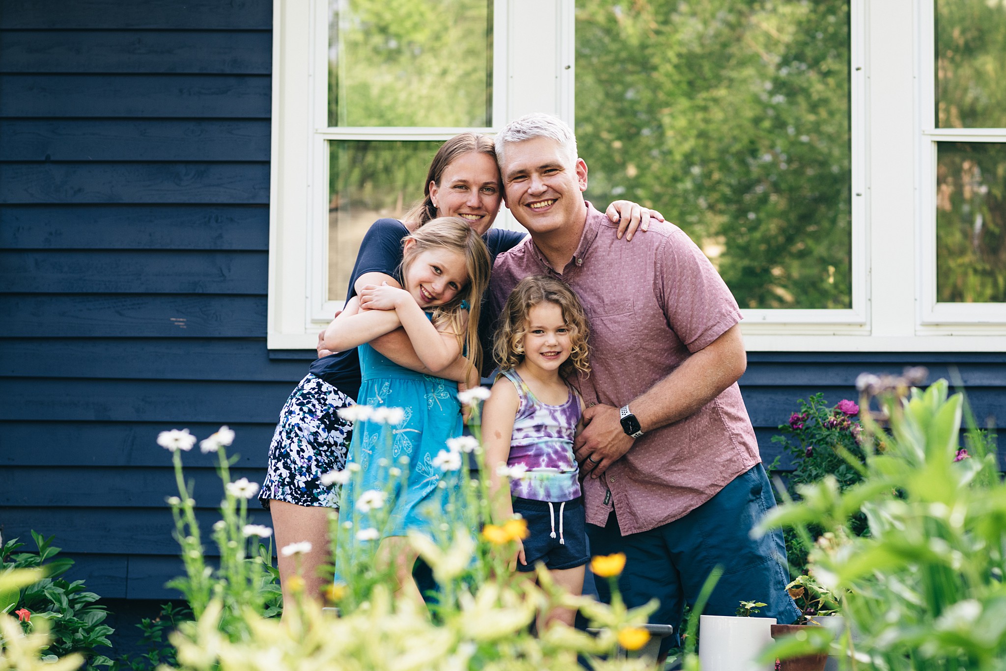 Family of four poses in front yard garden.