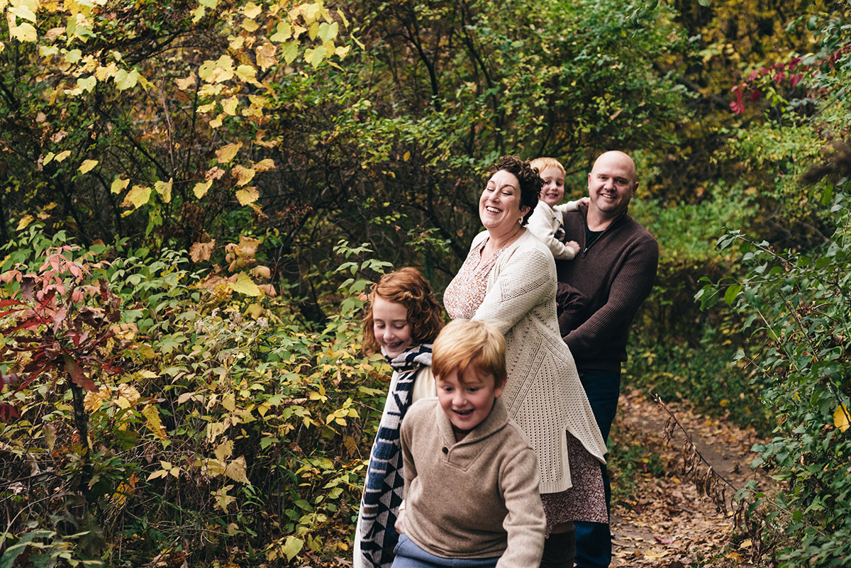 Family holds hands and runs through the woods.