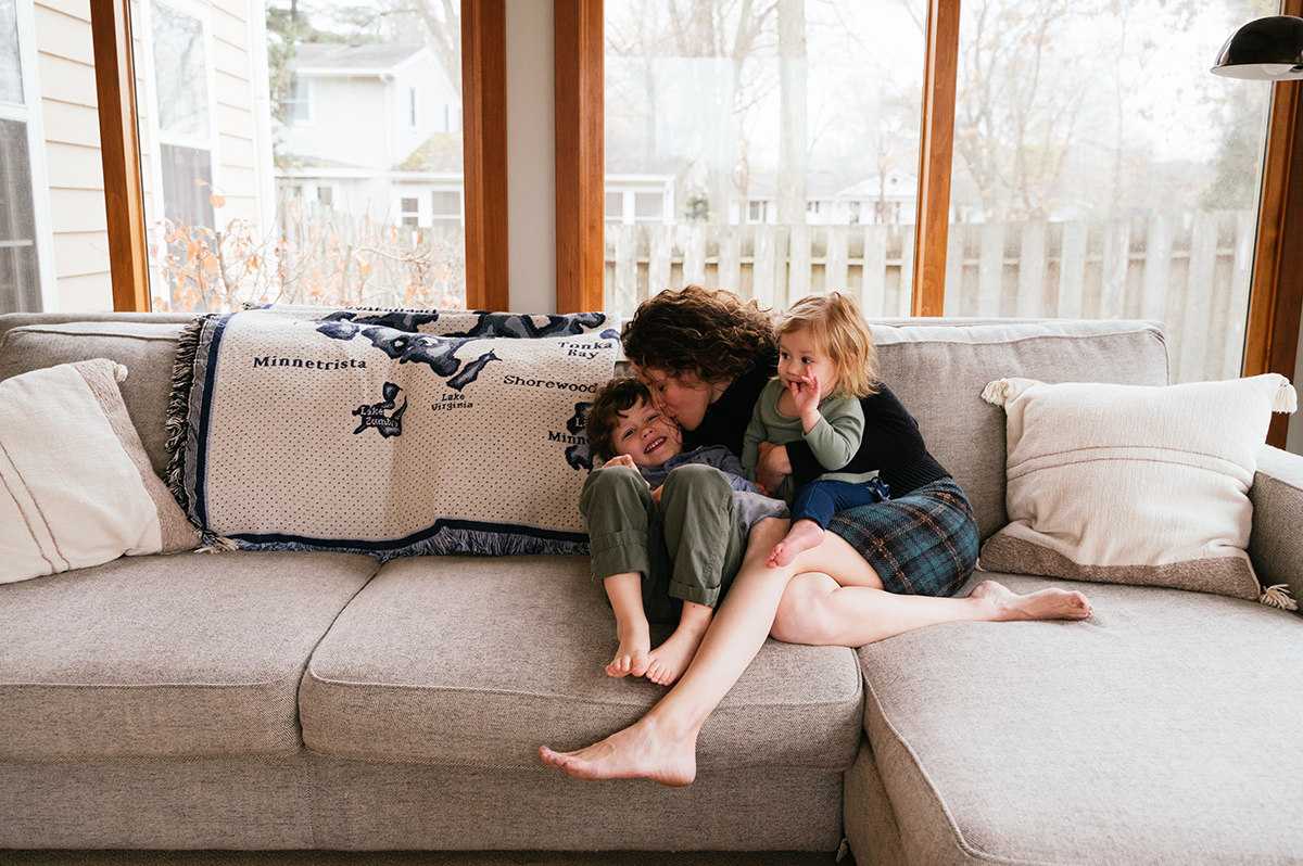 Mother snuggles and kisses her two kids while on a couch.