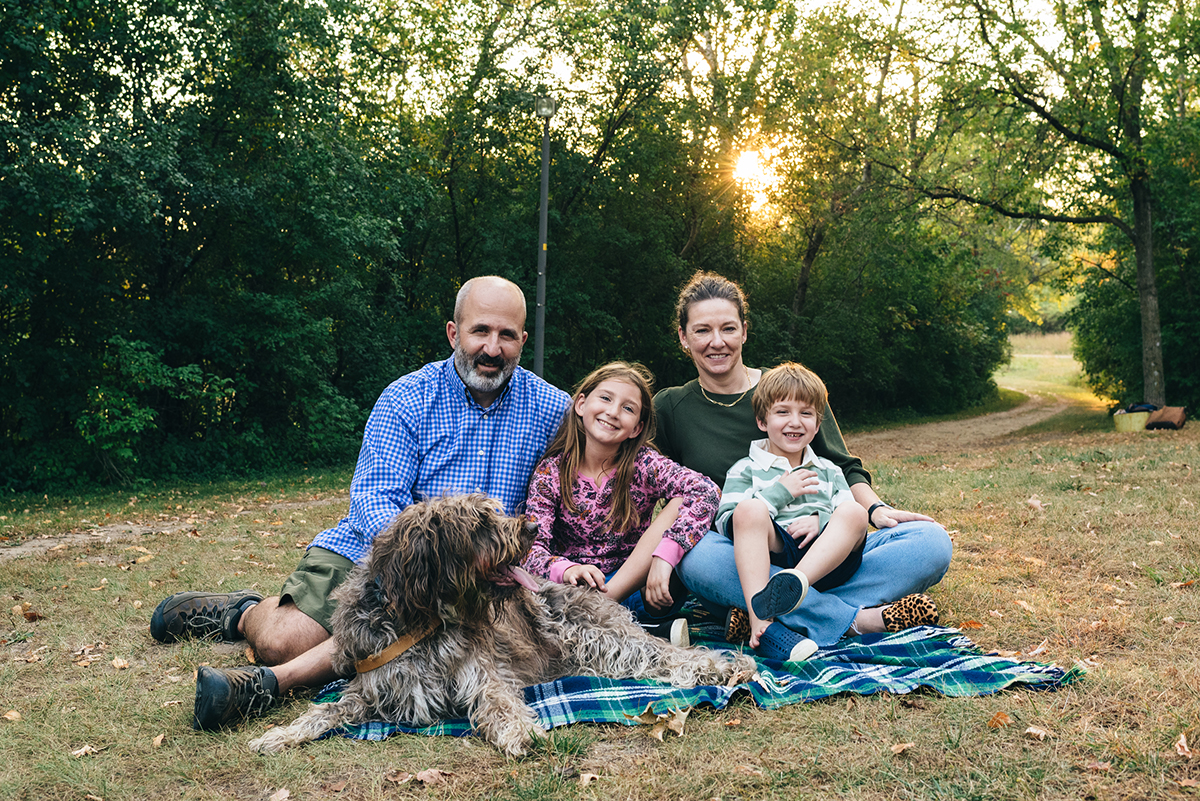 Family of four and dog giggle on blanket.