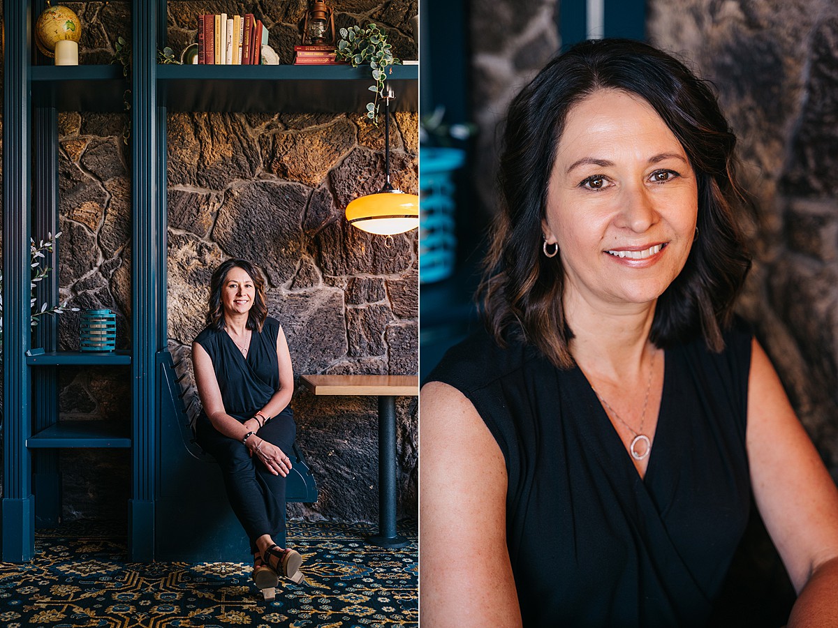 Woman sits in booth with brick wall background and smiles at camera.