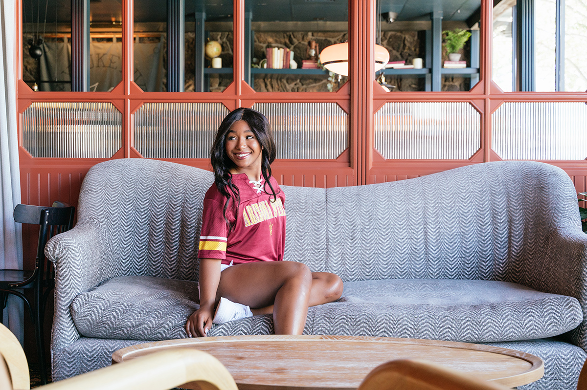 High school senior sits on a couch near beautiful windows.