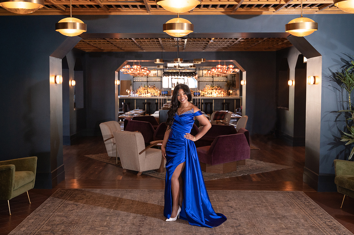 High school girl stands in lobby of High Country Motor Lodge in ball gown.