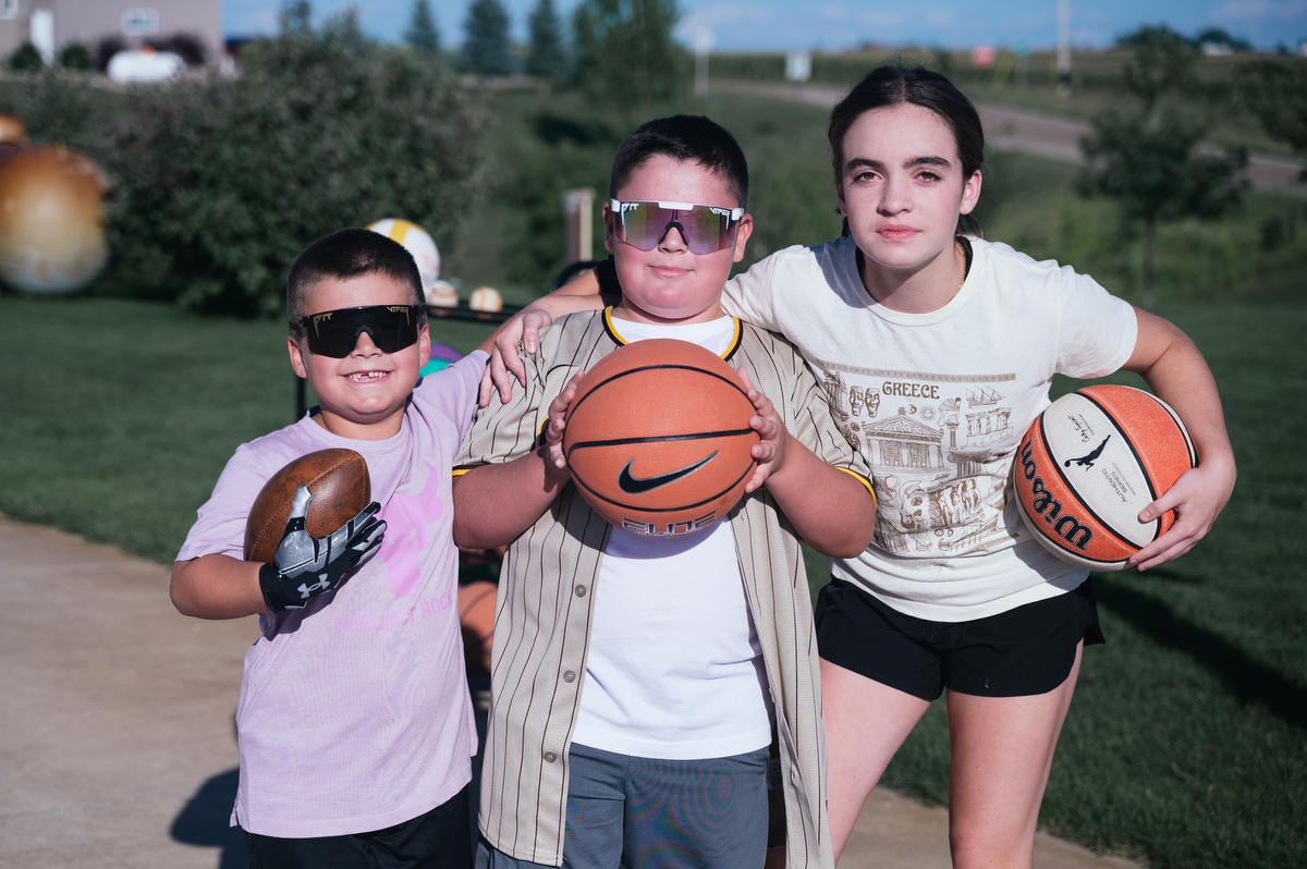 Three kids with basketballs look at the camera and smile.