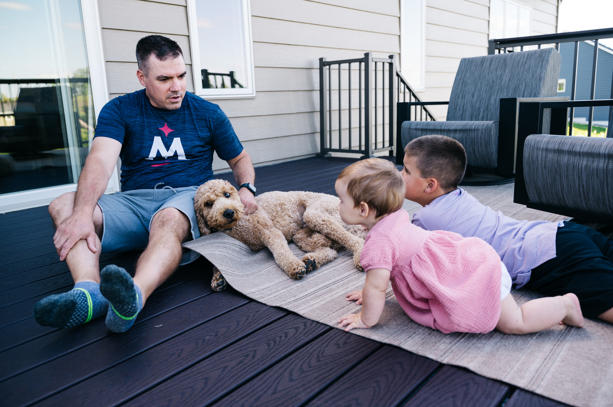Dad sits on the deck with son, daughter and dog playing during Northwest Minnesota family film.