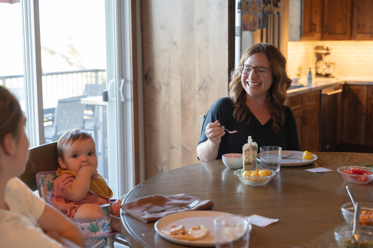 Mom laughs at toddler daughter while she eats dinner.