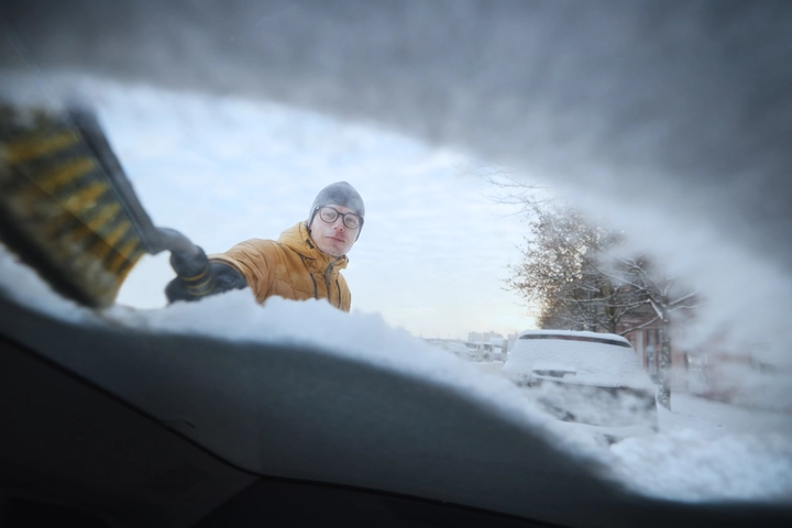 Man using a snow brush to wipe snow off of his windshiled Man using a snow brush to wipe snow off of his windshiled