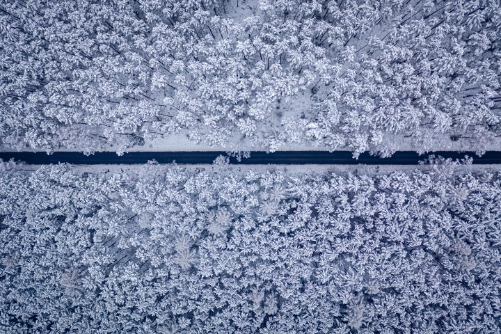 Birds eye view of a car driving down a snow covered highway surrounded by a forrest. Birds eye view of a car driving down a snow covered highway surrounded by a forrest.