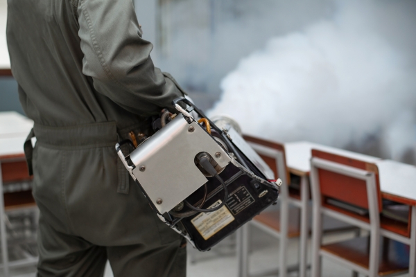 Person in protective gear using a fogging machine to spray insecticide in a classroom to combat dengue-carrying mosquitoes. Person in protective gear using a fogging machine to spray insecticide in a classroom to combat dengue-carrying mosquitoes.