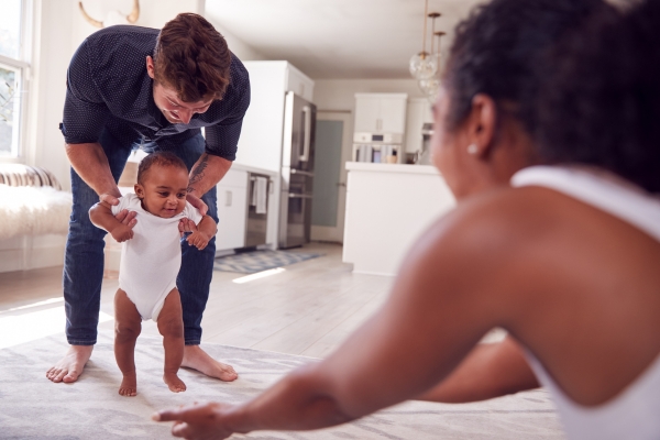 Baby attempting to take steps with parental support in a bright, modern home, illustrating milestones in walking development.