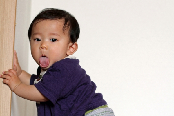 Baby pulling up to a standing position while playfully sticking out their tongue, illustrating early walking readiness and developmental milestones.