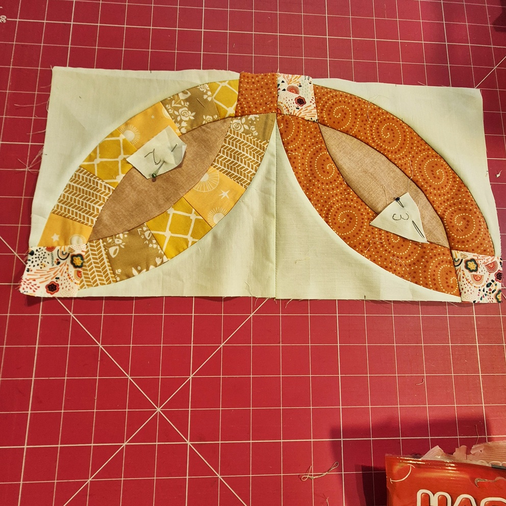 Double Wedding Ring patchwork blocks in orange and yellow fabrics, partly pieced on a mint green background, laid out on a pink cutting mat. Double Wedding Ring patchwork blocks in orange and yellow fabrics, partly pieced on a mint green background, laid out on a pink cutting mat.