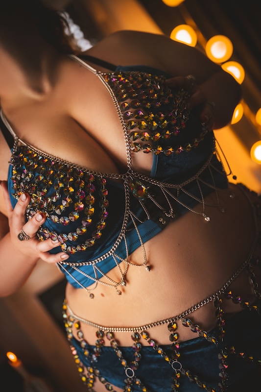 Close-up boudoir photography of a woman wearing a jeweled blue lingerie set with chains and embellishments, celebrating body confidence and self-expression.