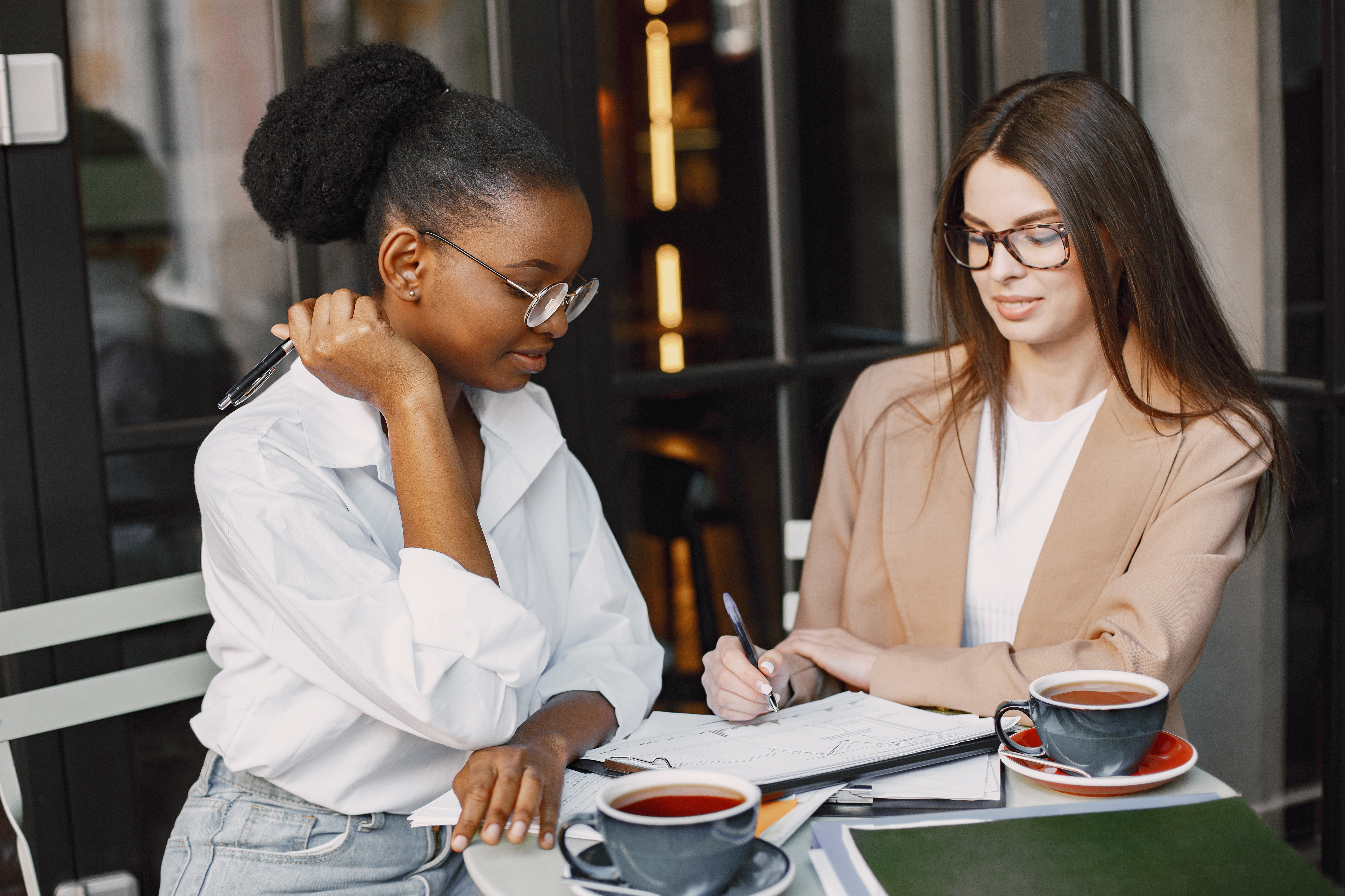 Two women sitting at an outdoor café table, engaged in a discussion. Two women sitting at an outdoor café table, engaged in a discussion.